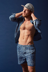 Image showing Fashion, body or model with six pack in studio on a blue background in an open unbuttoned shirt. Thinking, chest or handsome male person posing on color wall for masculine style with a trendy cap