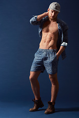Image showing Fashion, portrait or model with six pack in studio on a blue background in an open unbuttoned shirt. Body, chest or handsome male person posing on color wall for masculine style with a trendy cap