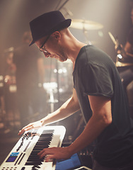 Image showing Concert, musician and man on piano at stage for performance, rock band or audio at music festival. Artist, professional or play on electric keyboard, synthesizer instrument or sound for entertainment