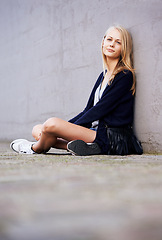 Image showing Fashion, portrait and woman by wall in city, relax and outdoor alone. Beauty, style and young person in urban town, casual clothes and blonde girl sitting on the ground on mockup space in Switzerland