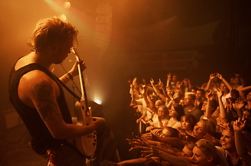 Image showing Guitar, concert and crowd at stage with man in performance of rock, metal and music. Festival, event and audience of people in celebration of talent in theater at night with spotlight and energy