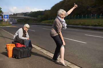 Image showing Women, road and funny hitch hiker for travel in retirement, lift and senior friends in city with bags for adventure. Elderly, thumbs up and tired by roadside with comic and stop transport to commute