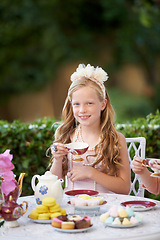 Image showing Girl, kid and portrait in garden with tea party for birthday, celebration and playing outdoor with cake. Person, child and face with happiness in backyard of home or house with cup or flower in hair