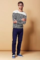 Image showing Fashion, crossed arms and portrait of man on beige background in trendy, stylish and casual clothes. Happy, attractive and person with stripe style for positive attitude, pride and smile in studio