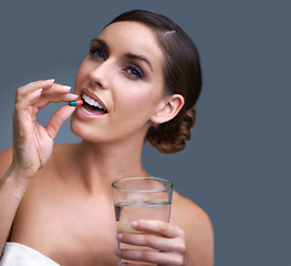 Image showing Woman, pill and water for healthcare, medication or drugs on a blue studio background. Female person. brunette or model with antibiotic, pharmaceuticals or vitamin supplement for wellness on mockup