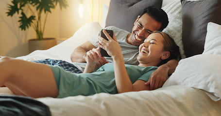 Image showing Asian couple, phone and social media for communication and entertainment on bed to relax, laughing and watch funny videp in bedroom at home. Man and woman using 5g internet while lying together