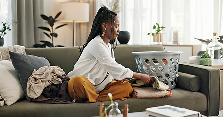 Image showing Laundry, housework and a black woman folding washing on a sofa in the living room of her home to tidy. Smile, relax and a happy young housewife cleaning her apartment for housekeeping or hygiene