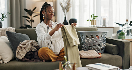 Image showing Laundry, housework and a black woman folding washing on a sofa in the living room of her home to tidy. Smile, relax and a happy young housewife cleaning her apartment for housekeeping or hygiene