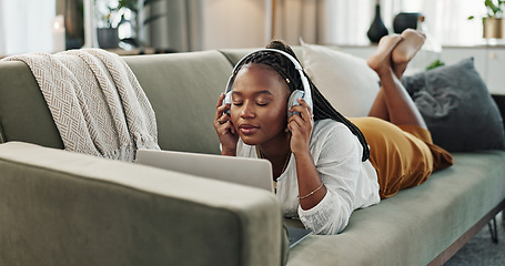 Image showing Home, headphones and black woman on a couch, laptop and typing with connection, internet and streaming music. African person, apartment and girl on a sofa, pc and headset with sound, song and audio
