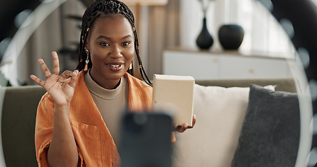 Image showing Wave, live streaming and happy black woman with box or product in home living room. Hello, influencer and person with package, record video on social media and content creation, ring light and phone