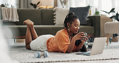 Image showing Laptop, coffee and woman on the floor in living room of modern apartment reading information. Technology, relax and young African female student study and drink latte on computer in lounge at home.