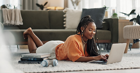 Image showing Laptop, typing and woman laying on the floor in the living room of modern apartment. Technology, elearning and young African female university student studying on a computer in the lounge at home.