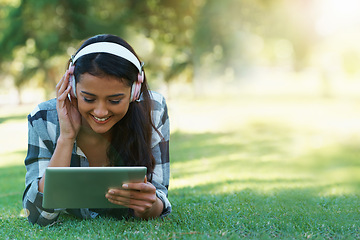 Image showing Woman, headphones and streaming music on grass, radio and internet for podcast on tablet in outdoors. Female person, happy and relaxing on lawn, weekend playlist and subscription to movie or series