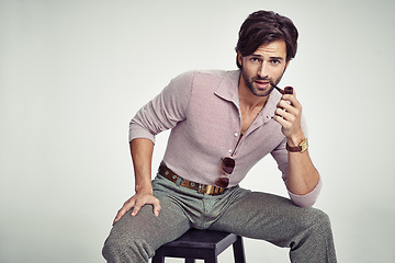 Image showing Fashion, man and portrait or pipe in studio with retro vintage, hipster outfit and confidence on chair. Model, person and face with 70s style, mock up space and calm expression with white background