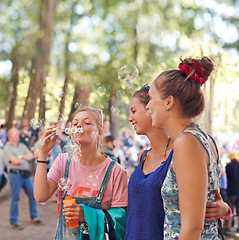 Image showing Festival, woman and friends blowing bubbles outdoor at event or party for celebration in summer. Smile, event and happy young people in nature or forest for concert, entertainment or performance