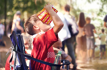 Image showing Festival, party and boy eating popcorn outdoor in summer at event for celebration or entertainment. Kids, food or snack and young child eating from box in nature, forest or woods alone with chair