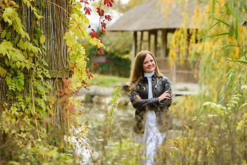 Image showing A young beautiful girl walks in the forest near a pond and looks happily into the frame