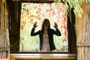 Image showing A young beautiful girl stands in the doorway of an old hut and looks into the frame through a non-existent glass