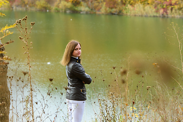 Image showing A girl stands by the lake on a warm autumn day, turned around and looked into the frame