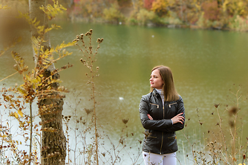 Image showing A girl stands by the lake on a warm autumn day and looks thoughtfully into the distance.