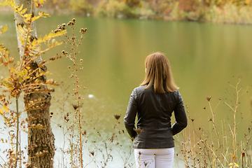 Image showing A girl stands by the lake on a warm autumn day, view from the back