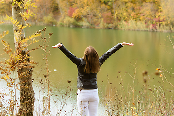 Image showing The girl by the autumn lake joyfully raised her hands up