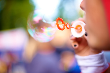 Image showing Closeup, blowing bubbles and outdoor with woman, summer and weekend break with event. Party, person and girl in a park and happy with soap toy and bokeh background with nature, rainbow and festival