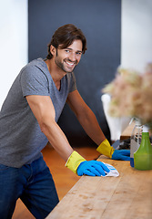 Image showing Happy man, portrait and cleaning table for housekeeping, hygiene or disinfection on furniture or surface at home. Male person, maid or cleaner and gloves for wiping, bacteria or germ removal at house