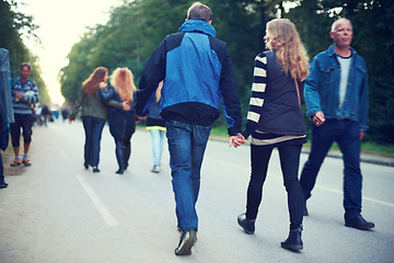 Image showing Couple, back and holding hands while walking among trees and crowds along road in New Zealand. Rear view of man, woman and people for travel, date and bonding in busy woods, park and highway