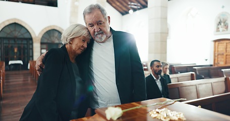 Image showing Funeral, coffin and senior couple hug in church for goodbye, mourning and grief in memorial service. Depression, sad family and man embrace woman by casket for greeting, loss and burial for death