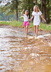 Image showing Mother, daughter and happiness outdoor in river for bonding, support or holding hands on holiday in nature. Family, woman and girl child with smile or adventure on vacation, travel and lake with love