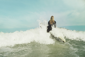 Image showing Ocean, wave and splash with surfer woman in wetsuit for sports, fitness or exercise in summer from back. Blue sky, sea and surfing with person on surfboard in water for travel, vacation or holiday