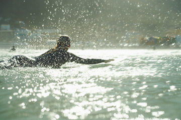 Image showing Swimming, splash and woman on surfboard in ocean for fitness, exercise or recreation in summer. Sports, travel or training with surfer person in sea for vacation, holiday or leisure hobby from back