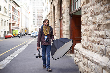 Image showing Camera, equipment and photographer in city for photoshoot with lighting gear on street. Cameraman, walking and professional photography tools for press, project and person travel with technology