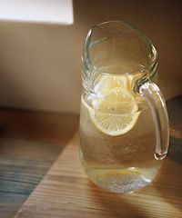 Image showing Water, lemon and jug in kitchen for wellness or detox drink for hydration or natural vitamins, organic or counter. Beverage, sunshine and glass in home for healthy antioxidants, vitamin c or immunity