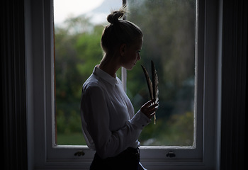 Image showing Woman, feather and window in home for writing in dark room and mysterious aesthetic for artistic pose. Female writer, dim light and ink pen with thinking, author and old school setting for creativity