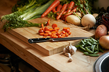 Image showing Vegetables, carrots and wood board for cooking in kitchen with onion or potato, leafy green or nutrition. Knife, garlic and counter for healthy wellness or salad diet for vegan dish, fibre or recipe