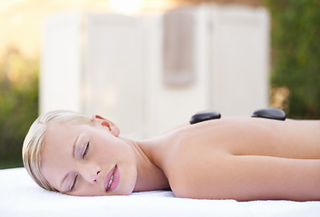 Image showing Spa, woman and hot stone on massage bed with peace for wellness, zen and beauty treatment for body care. Person, relax and stress relief at resort, salon table and luxury on holiday or vacation