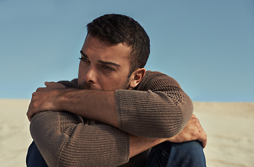 Image showing Depressed, model or man in the desert thinking of travel in summer sitting on holiday vacation. Upset, worry or stress with face of nervous person on the ground or sand dunes with anxiety or fear