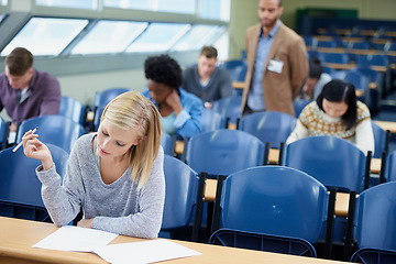 Image showing Exam, classroom and student with pen for thinking, assessment and writing at campus. Woman, planning and sitting with paper for brainstorming, education and growth of knowledge in university class