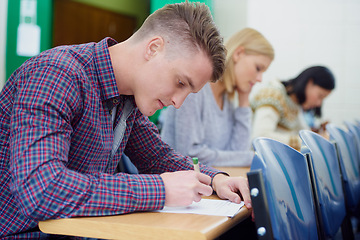 Image showing University student, desk and writing exam in classroom for education assessment for knowledge, diploma or scholarship. Men, woman and test in London lecture hall or study document, academy or college