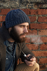 Image showing Face, winter and pipe smoke with man outdoor on wall background for fashion, style or clothing. Morning, tobacco or habit and young person with beanie smoking in cold weather season to relax