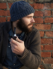 Image showing Man, pipe and thinking by brick wall for planning, ideas or smoking in winter with beanie on head. Male person, fashion and tobacco for style, vision or contemplating outdoors on cold morning