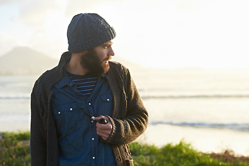 Image showing Man, pipe and thinking in nature by ocean for ideas, vision or planning on winter morning. Male person, sunrise and standing on grass by sea for relaxation, wondering or smoking with tobacco outdoors