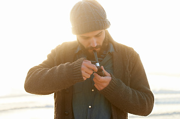 Image showing Smoker, man and lighting a pipe in outdoor, relax and sailor habit on winter morning in sunrise. English guy, nicotine addiction or vintage smoking for flavor, taste or vacation by ocean in cape town