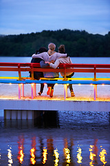 Image showing Lake, bench and back of girl friends watching water in nature on vacation, adventure or holiday. Bonding, care and female friends embracing on wood chair in evening on outdoor weekend trip together.