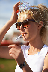 Image showing Crown, smoking and young woman with cigarette in nature at outdoor festival, event or party. Fun, tiara and female person with tobacco, sunglasses and casual fashion in outside park or field.