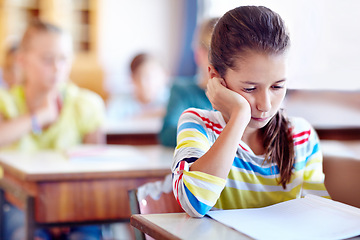 Image showing Child, school and desk with book or bored in classroom or education lesson or reading, knowledge or studying. Girl, kids and unhappy or learning or tired pupil with paper or fatigue, student or moody