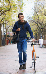 Image showing Man, walking and push bicycle in city to travel on eco friendly transport outdoor, commute or trip. Cycling, person and bike in urban town, street or road for journey at sidewalk of park with bag