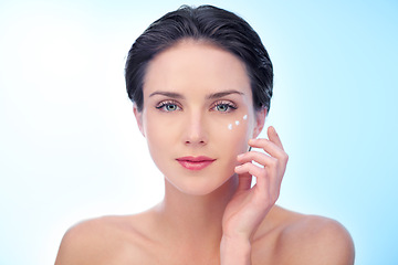 Image showing Woman, portrait and moisturizer application or cream for smooth skincare for treatment, dermatology or wellness. Female person, face and lotion on blue background in studio, mockup space or product